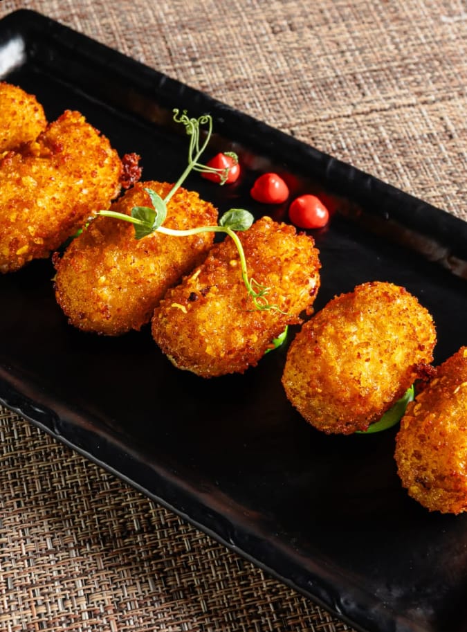 Croquetas doradas sobre bandeja negra con brotes y gotas de salsa roja