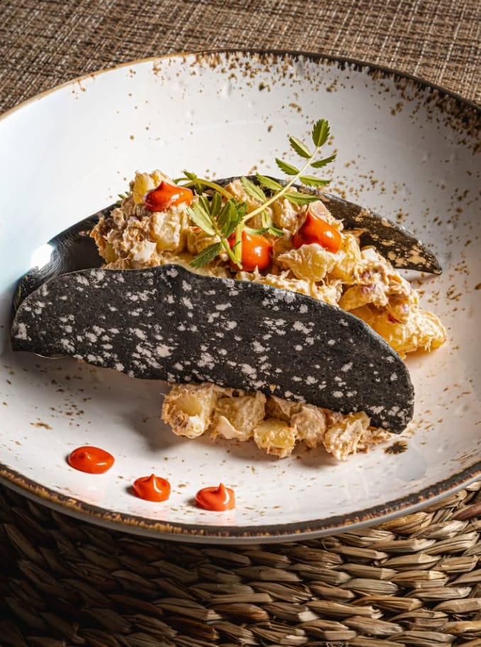 Ensaladilla con lámina de pan negro crujiente y puntos de salsa roja