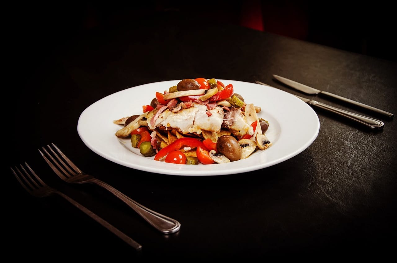 Pescado blanco con champiñones, tomate cherry y pepinillos en plato blanco