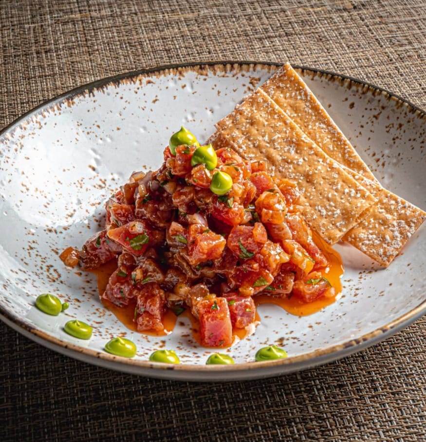 Tartar de atún con puntos de salsa verde y crujientes, en plato de cerámica